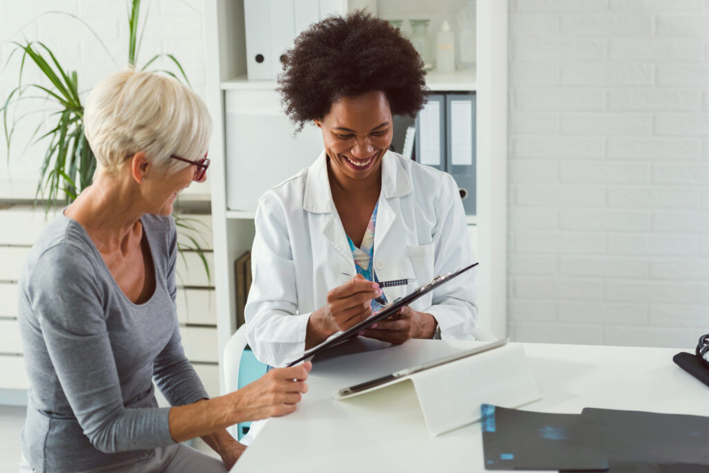 A female doctor sits at her desk and chats to an elderly female