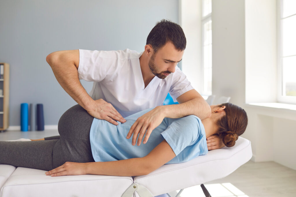 Man doctor chiropractor or osteopath fixing lying womans back in manual therapy clinic