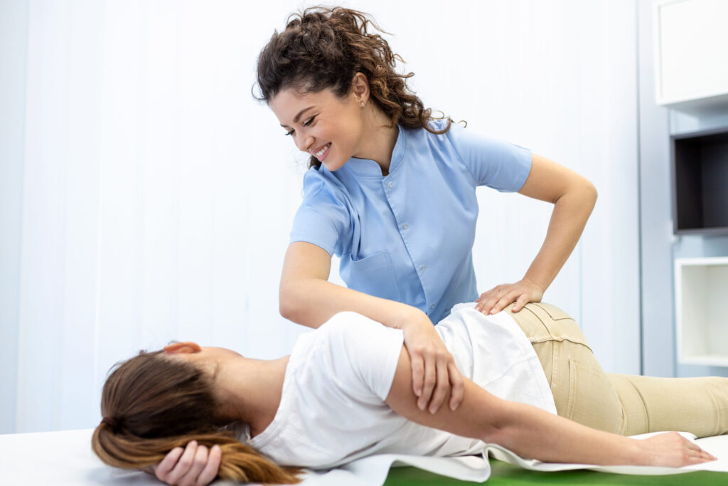 Young doctor chiropractor or osteopath fixing lying womans back with hands movements during visit in manual therapy clinic